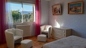A bedroom with a bed, a chair, a dresser, and a window with a view of trees and hills. - Beautiful Provencal Stone Villa with Large Pool and Pool House (Grasse)
