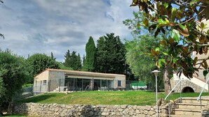 A stone building with a tiled roof, a covered outdoor area with seating, and a stone staircase leading to a door. - Beautiful Provencal Stone Villa with Large Pool and Pool House (Grasse)