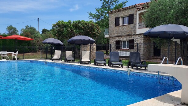 A swimming pool with lounge chairs and umbrellas, surrounded by a stone building and greenery. - Beautiful Provencal Stone Villa with Large Pool and Pool House (Grasse)
