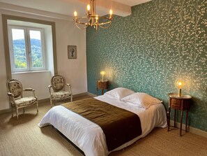A bedroom with a large bed, two chairs, a chandelier, and a view of greenery through a window. - Charming 17th century residence, Calm, Livradois Forez Natural Park, Olliergues (Olliergues)
