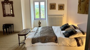 A bedroom with a large bed, a window with a view, a radiator, a wooden chair, and a mirror on the wall. - Charming 17th century residence, Calm, Livradois Forez Natural Park, Olliergues (Olliergues)