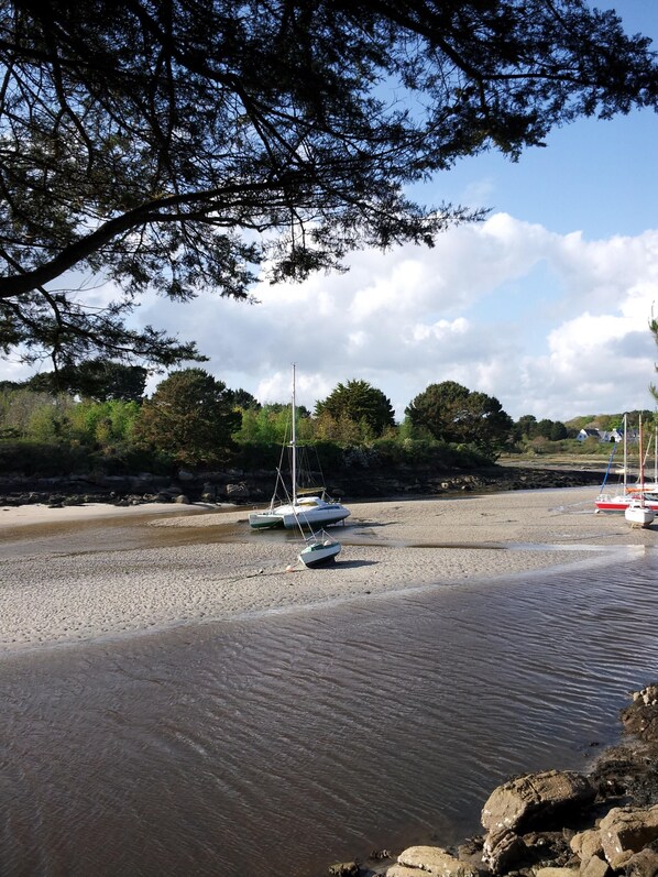 A beach with boats anchored in shallow water, surrounded by trees and a rocky shoreline. - New - Charming thatched cottage in the water with swimming pool (Pointe de Grignallou)