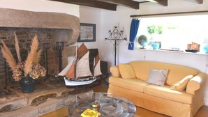 A cozy living room with a stone fireplace, a model ship, a glass coffee table, and a yellow sofa. - New - Charming thatched cottage in the water with swimming pool  (Pointe de Grignallou)