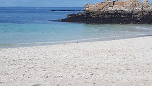 A beach with clear water, a rocky outcrop, and a distant sailboat. - New - Charming thatched cottage in the water with swimming pool  (Pointe de Grignallou)