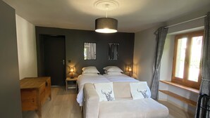 Une chambre à coucher avec un lit, des tables de chevet, un banc en bois, un tapis rouge et une fenêtre avec des rideaux.