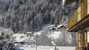 Un village enneigé avec des maisons en bois, une clôture en bois et un arbre recouvert de neige.