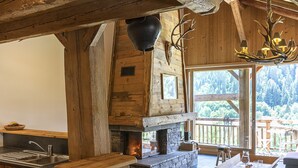 A rustic interior with exposed wooden beams, a stone fireplace, a wooden bar, and a large window overlooking a forested area. - Pags Haut, Pags Haut (Châtel)