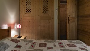 A wooden room with a bed, a nightstand with a lamp, and two wooden doors with louvered windows. - Pags Haut, Pags Haut (Châtel)