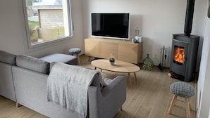 Een moderne woonkamer met een grijze bank, een televisie, een houten kast, een klein tafeltje en een houtkachel.