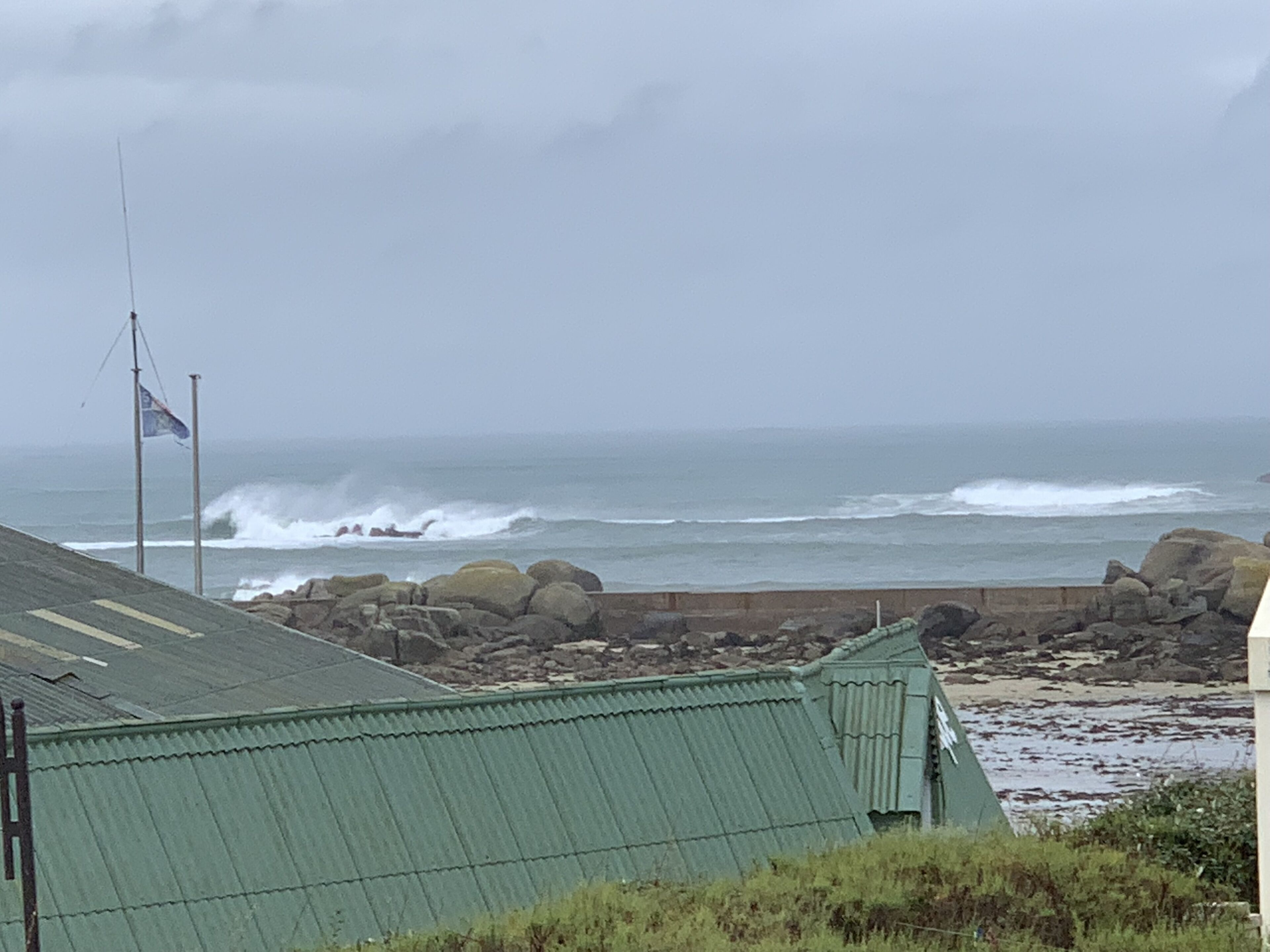 A coastal building with a green roof, a flag, and a rocky shoreline with waves.