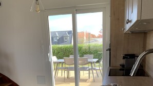 Een keuken met een houten aanrecht, een schaal met fruit, een spoelbak en uitzicht op buiten via een glazen deur.