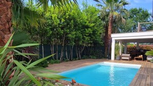 Une piscine entourée d’une végétation luxuriante, une terrasse en bois et un espace salon abrité.