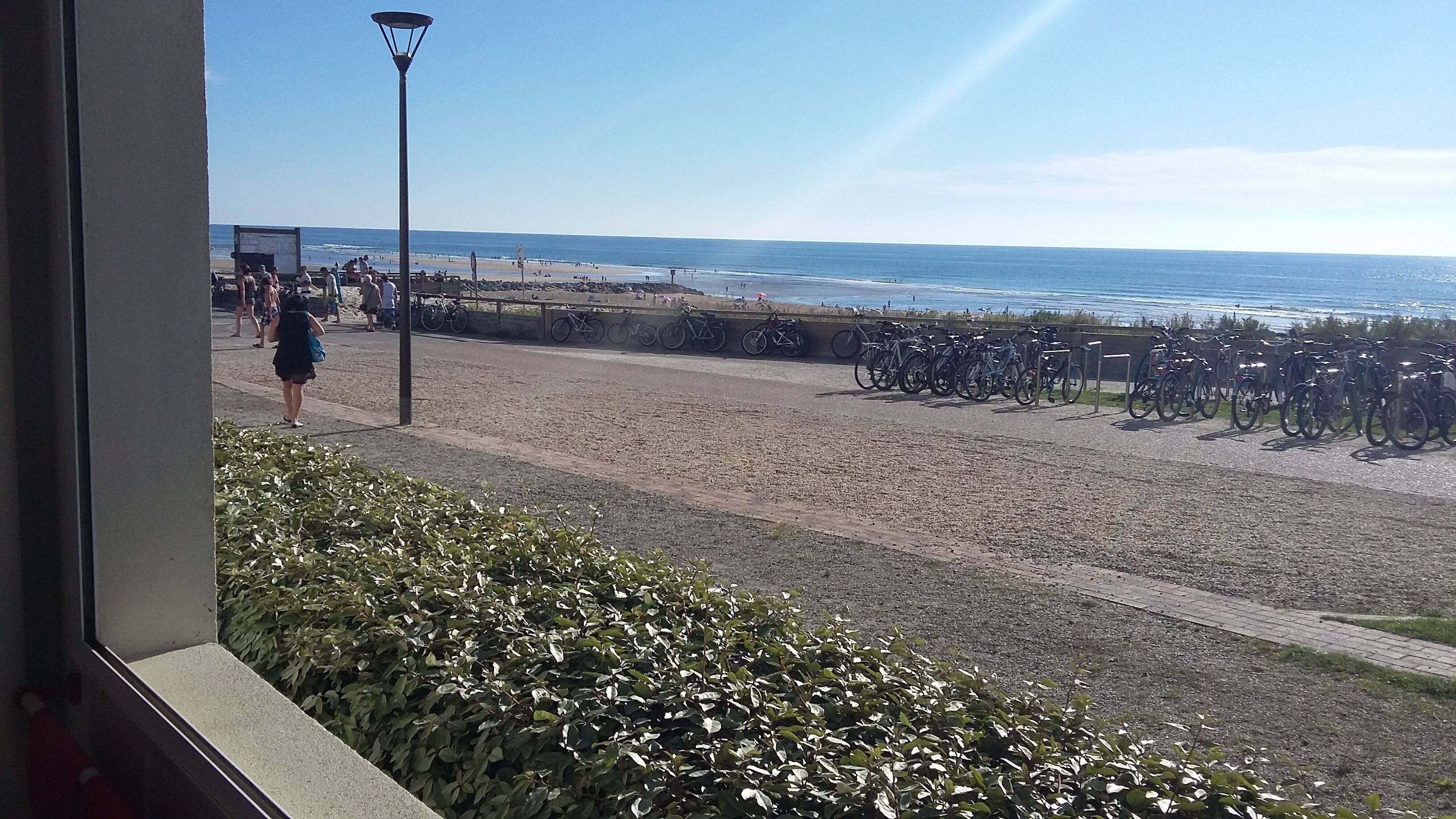 Una playa con bicicletas estacionadas a lo largo de la orilla, un farol y gente caminando.