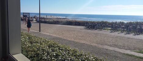 Una playa con bicicletas estacionadas a lo largo de la orilla, un farol y gente caminando.