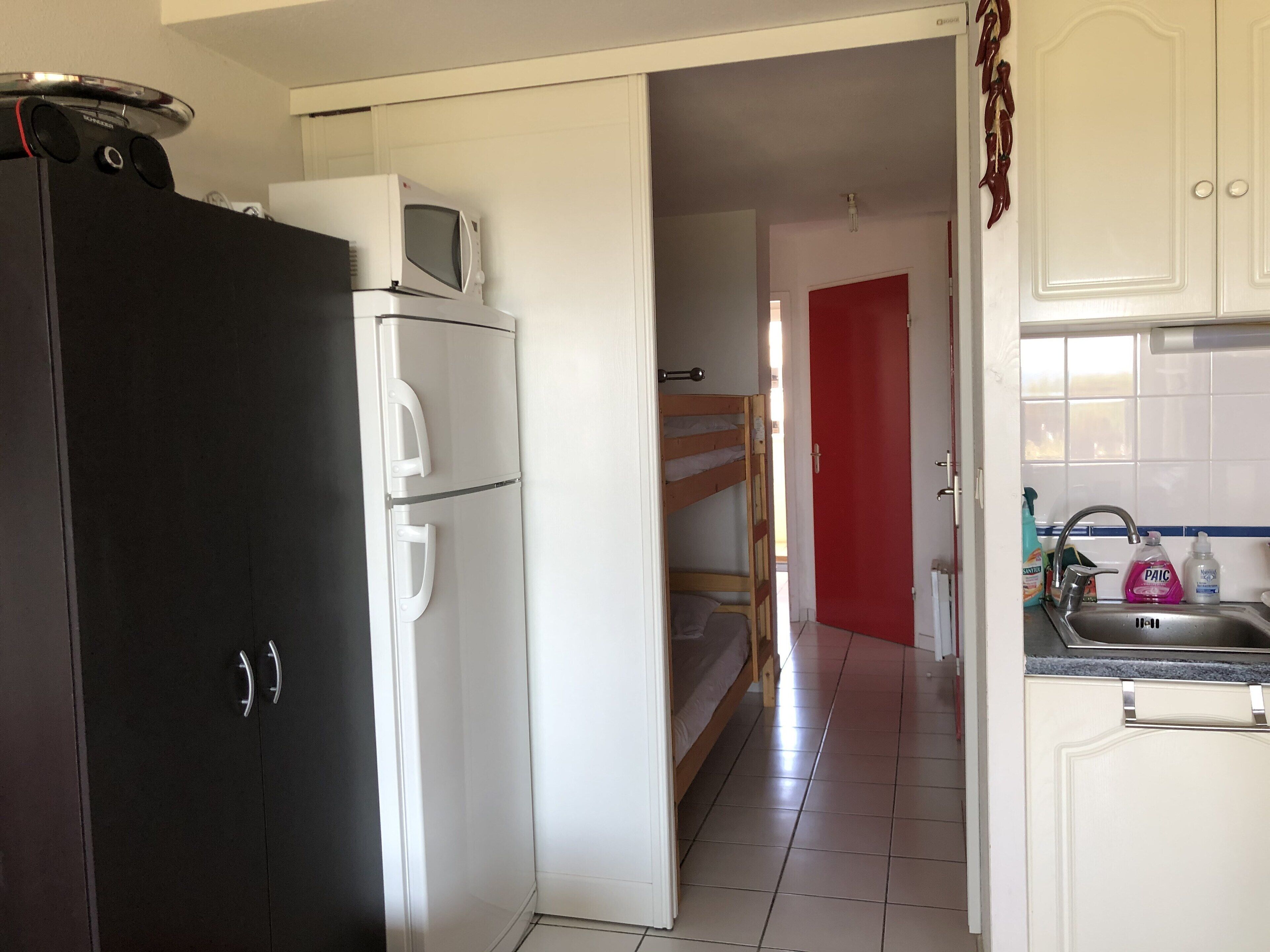 Una cocina con un refrigerador negro, un microondas blanco y una puerta roja al fondo.