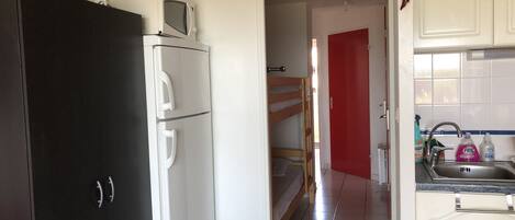 Una cocina con un refrigerador negro, un microondas blanco y una puerta roja al fondo.