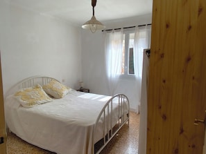 Een slaapkamer met een bed, nachtkastje, lamp en een raam met gordijnen.