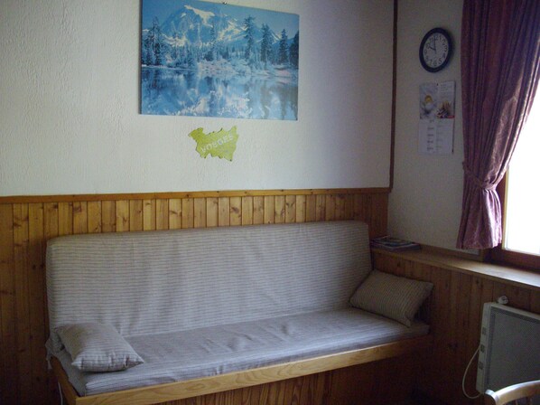 Um quarto com painéis de madeira, um sofá, um relógio e uma janela com cortinas.