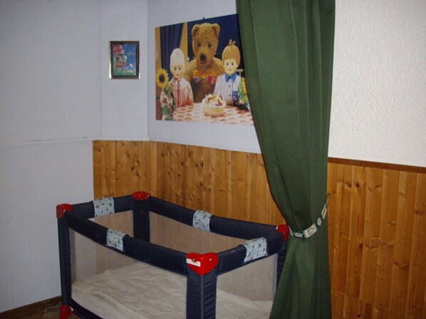 A room with a wooden panel wall, a crib with a heart-shaped top, and a painting of bears on the wall. - Chalet style apartment, quiet environment and mountain sports nearby (La Bresse)