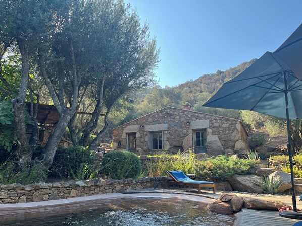 Une maison en pierre avec une piscine, entourĂ©e dâarbres et de rochers.