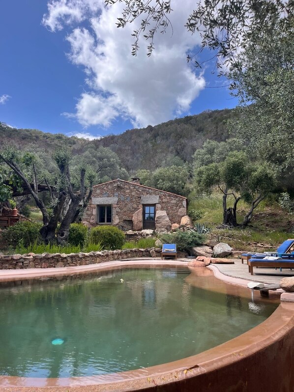 A stone house with a pool, surrounded by trees and hills.