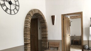 A room with a stone archway, a wooden door, a small table with a chair, and a round white object on a green table. - Quiet sheepfold near Palombaggia beach with private pool. (Porto-Vecchio)