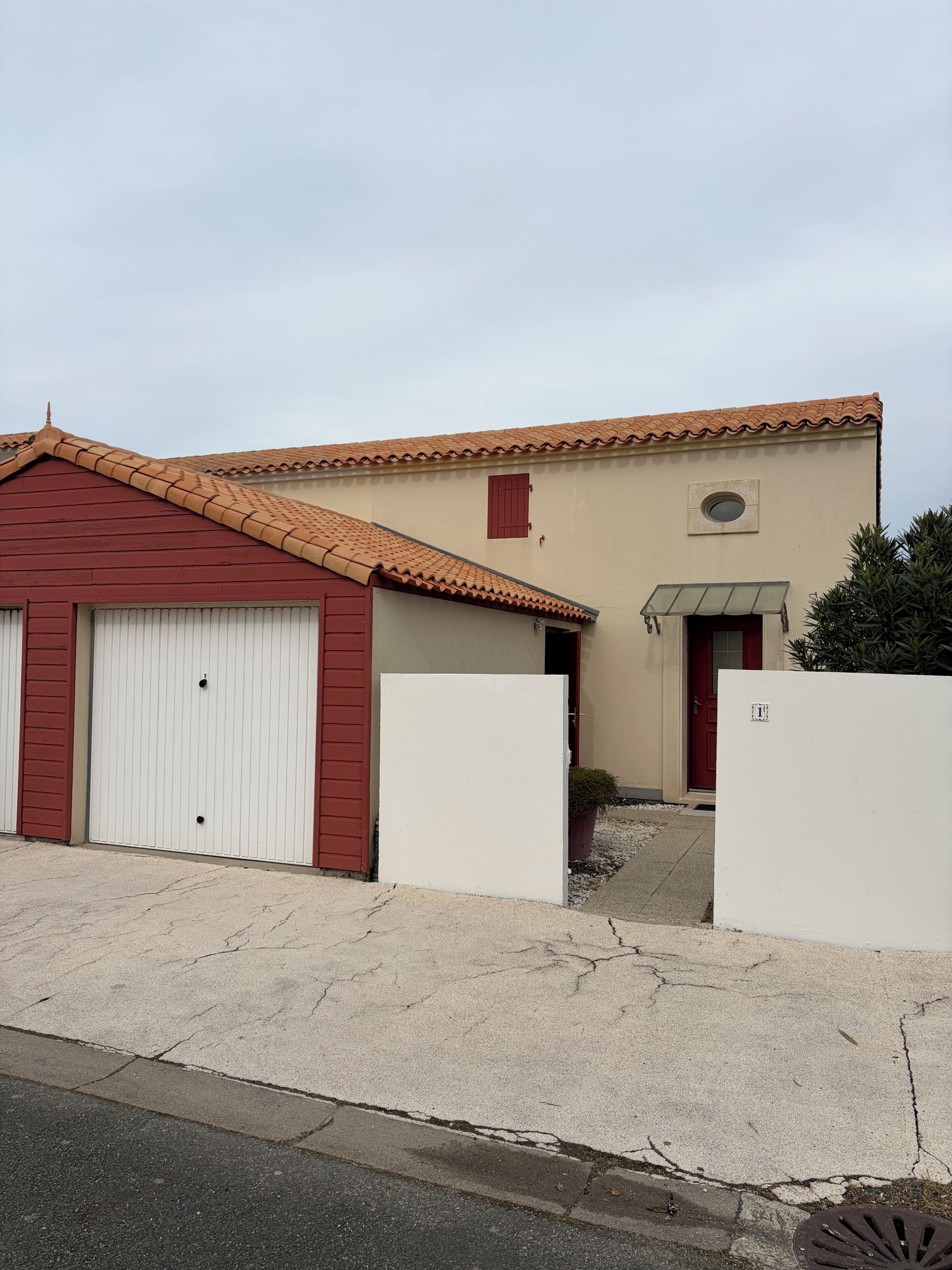 Un bâtiment à deux étages avec une porte rouge, un garage et un petit jardin.
