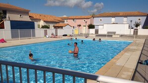 A swimming pool with people in the water, surrounded by a white fence and buildings in the background.