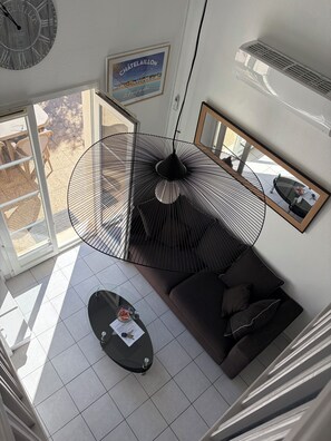 A modern living room with a large window, a black pendant light, a sofa, and a coffee table. - House in private residence with swimming pool and bicycles, 20 min walk from the beach (Châtelaillon-Plage)
