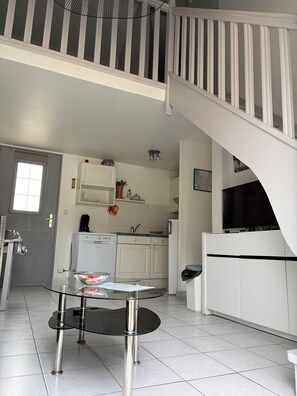 A modern kitchen with white cabinets, a glass table, and a staircase leading to an upper level. - House in private residence with swimming pool and bicycles, 20 min walk from the beach (Châtelaillon-Plage)