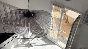 A room with a large window, a hanging fan, a clock, and a framed picture on the wall.