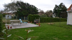 Un jardin avec une table de pique-nique, des chaises longues et un barbecue.