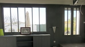 A room with large windows, a framed picture on a shelf, and a floor lamp. - Charming house close to the sea and cycle paths (Saint-Martin-de-Ré)