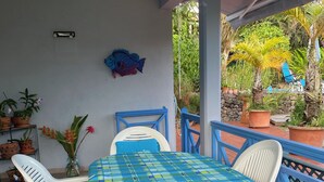 Ein überdachter Patio-Bereich mit Tisch und Stühlen, umgeben von Topfpflanzen und einer dekorativen Wandkunst mit Fischmotiv.