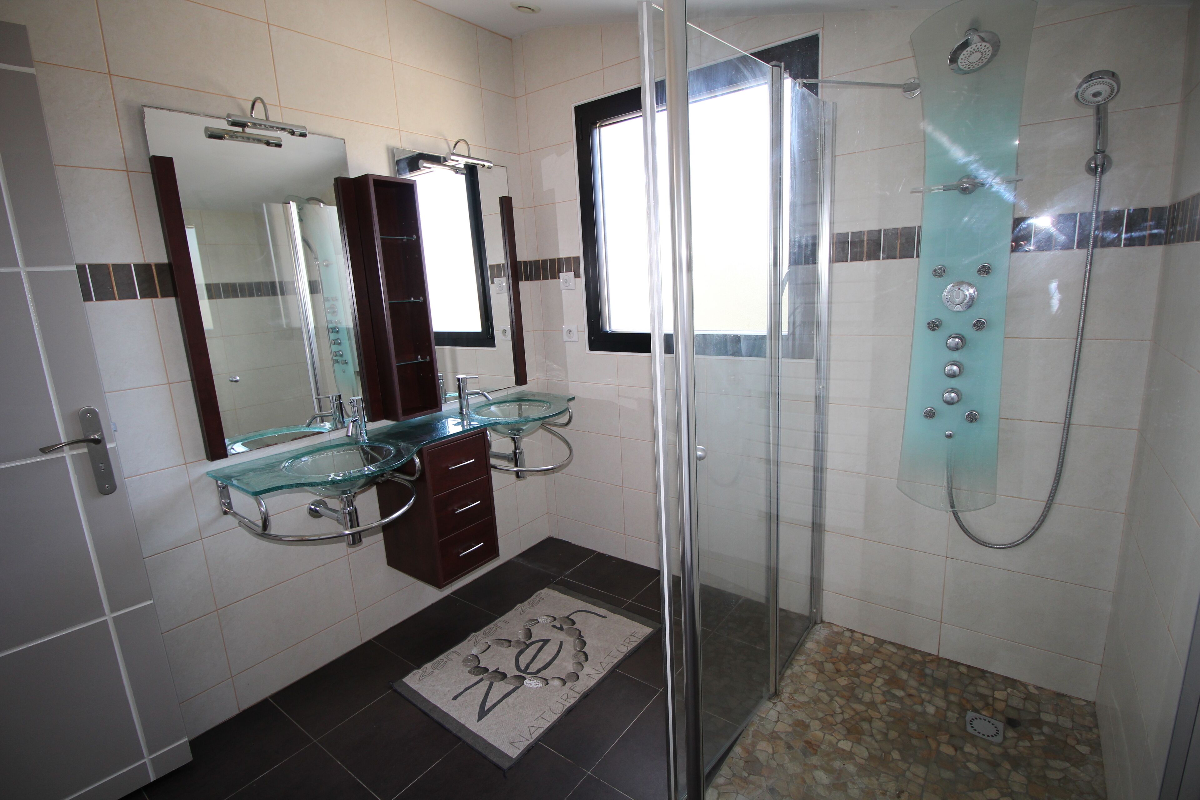 A modern bathroom with a glass shower enclosure, a glass sink, and a large mirror.