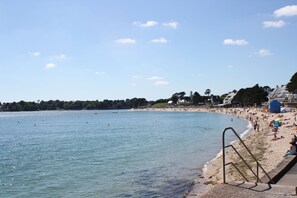 A beach with a clear sky, a sandy shore, and a few buildings in the background.