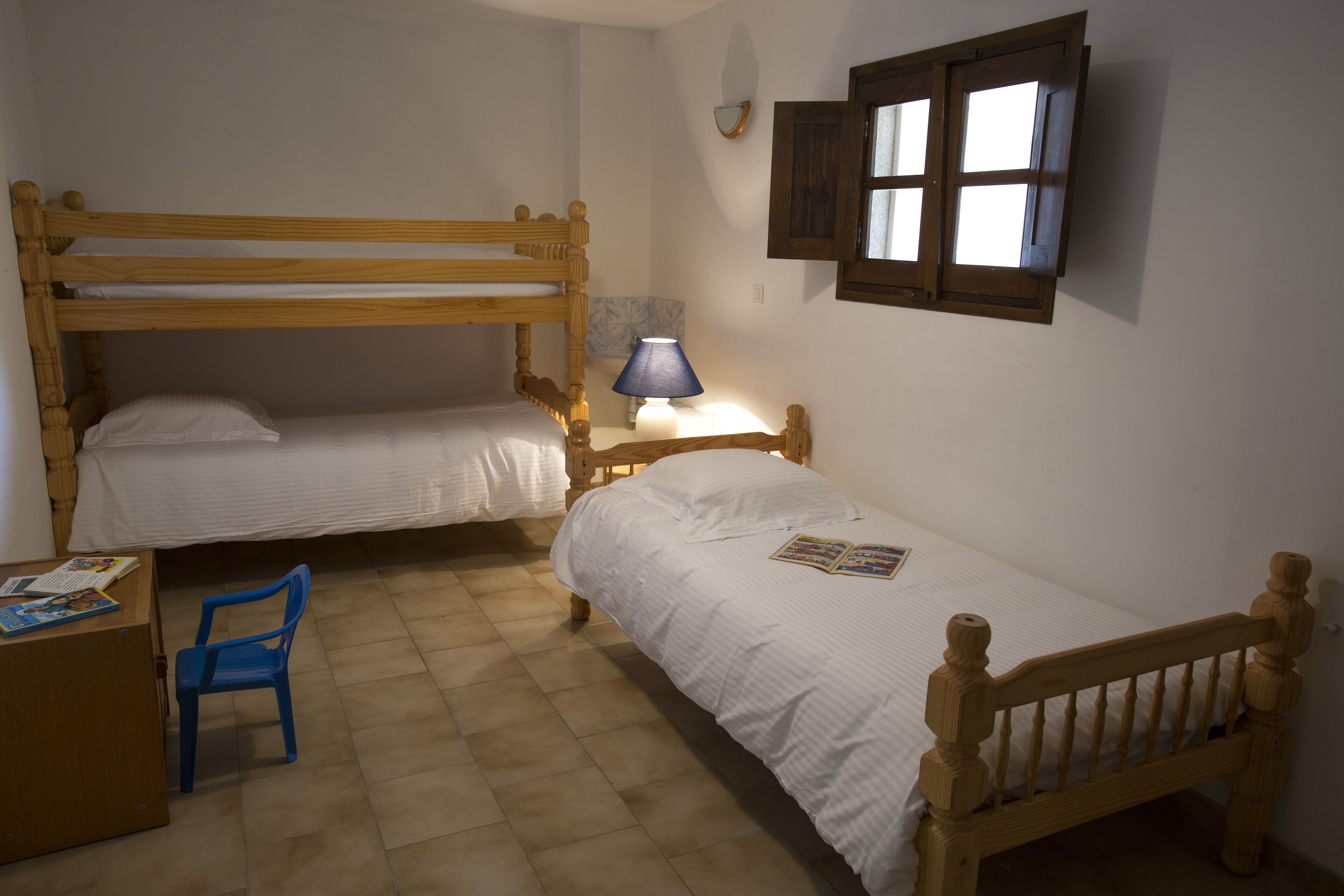 A room with two wooden bunk beds, a desk with a chair, a lamp, and a window.