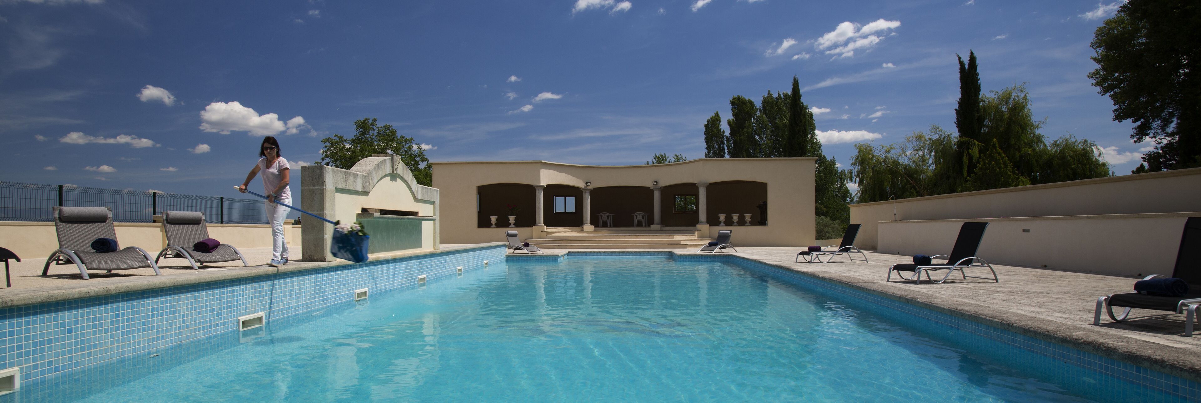 A swimming pool with lounge chairs and a person cleaning the pool.