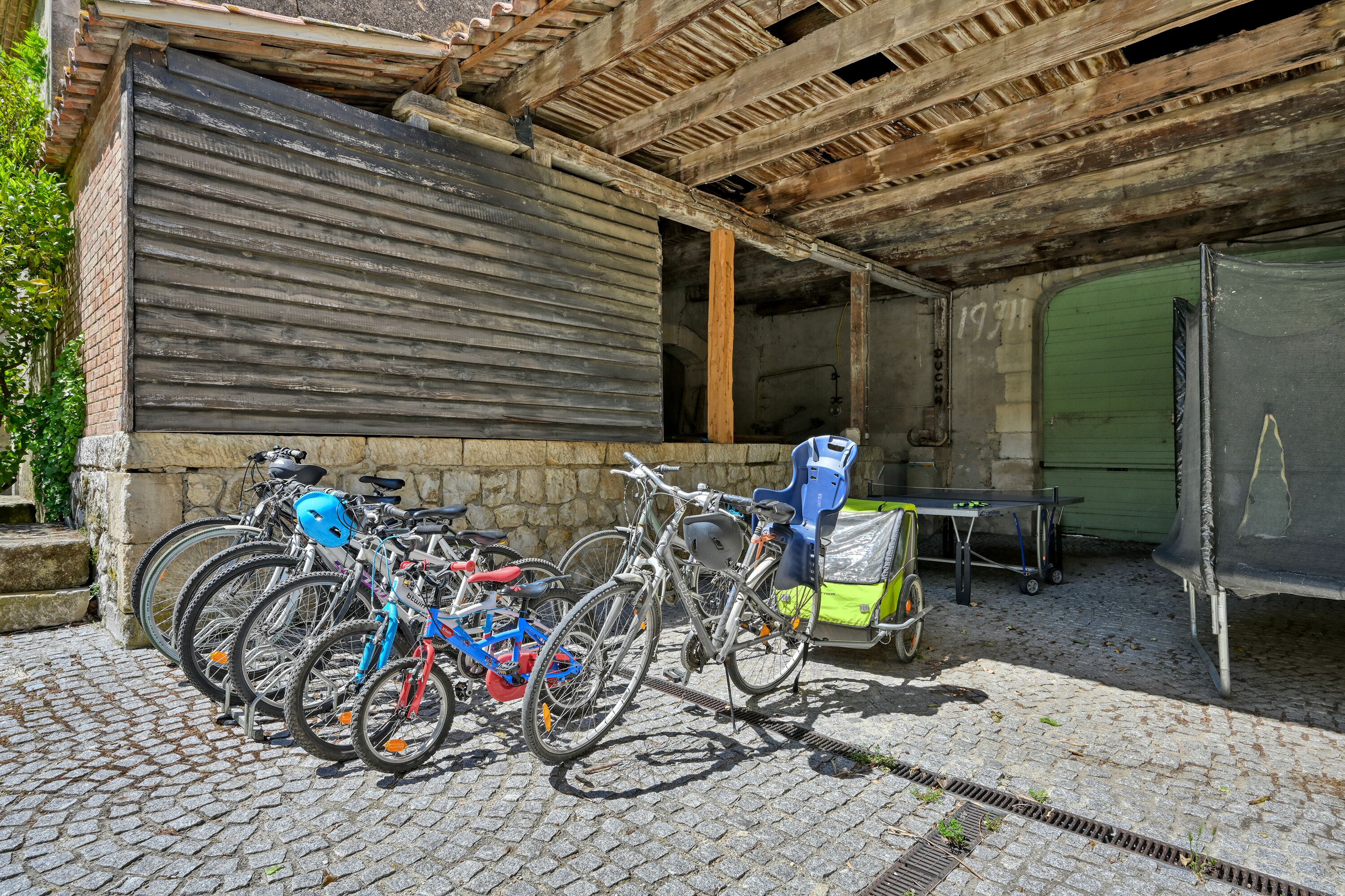 A covered outdoor area with bicycles parked against a wall, a green door, and a table with a chair.
