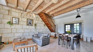 A spacious living area with a sofa, dining table, and chairs, a staircase, and a kitchen area with a window. - La Maison des Vendangeurs***, Gîte with swimming pool and bicycles  (Beaucaire)
