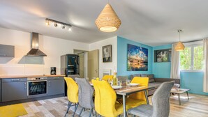 A modern kitchen with a built-in oven, a dining area with yellow chairs, and a large window with curtains.