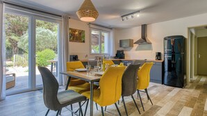 A modern kitchen with a dining area, large windows, and a view of greenery.
