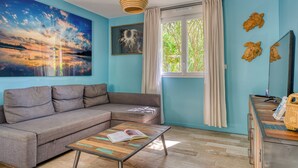 A living room with a sofa, a coffee table, a painting, a window with curtains, and a wall-mounted mirror.