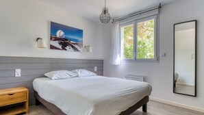 A bedroom with a bed, bedside table, wall-mounted lamp, window, and a painting.
