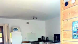 A compact kitchen with a wooden table and chairs, a microwave on a white fridge, and a coffee machine. - Charmante maison au coeur du village /Charming house in the heart of the village (Wissant)