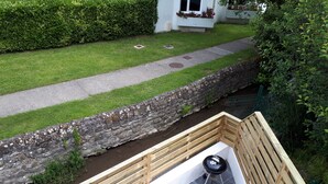 A patio area with a stone retaining wall, a wooden deck, and a white outdoor table and chairs. - Charmante maison au coeur du village /Charming house in the heart of the village (Wissant)
