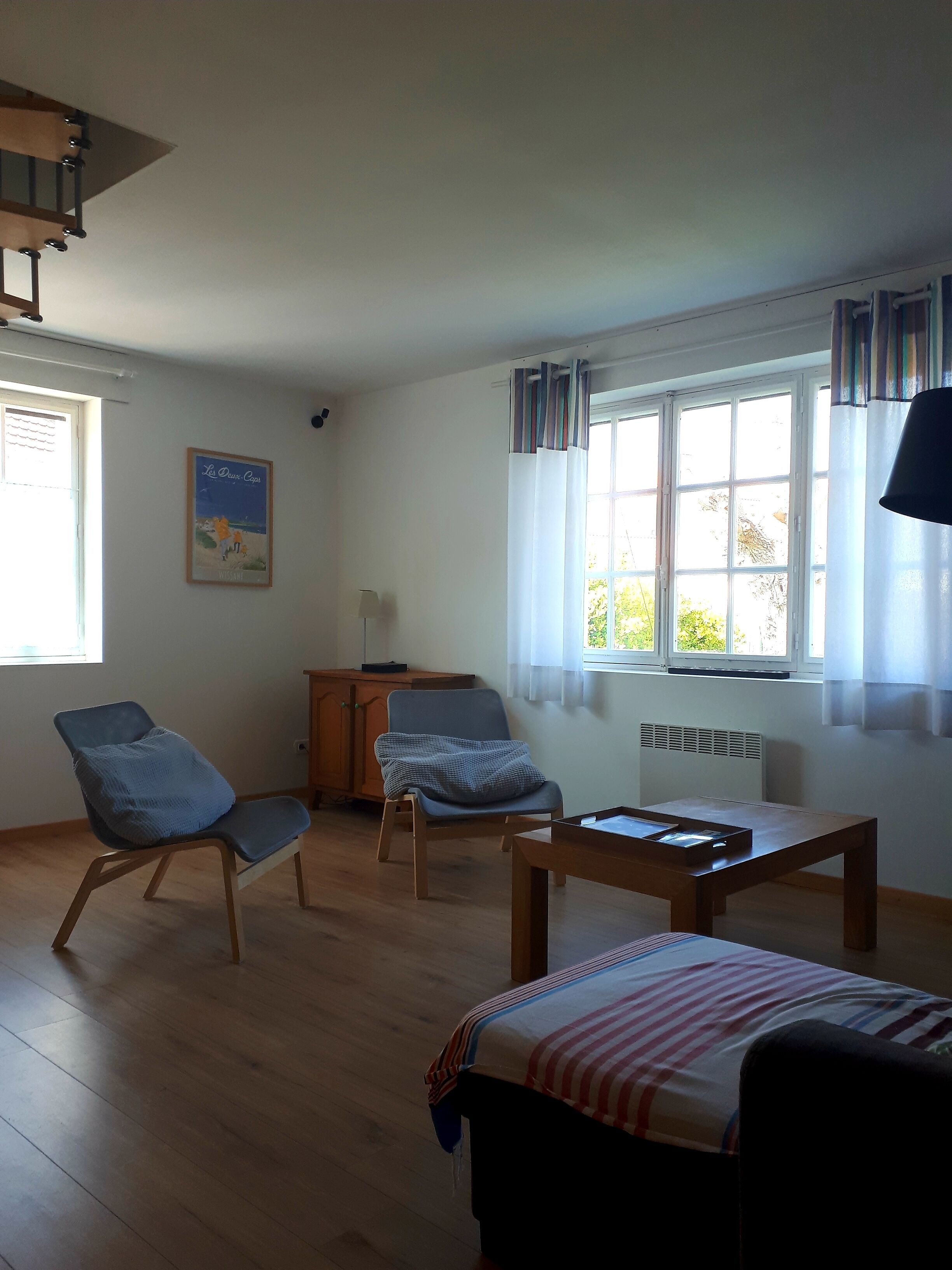A room with a bed, two armchairs, a wooden table, a radiator, and a window with curtains.