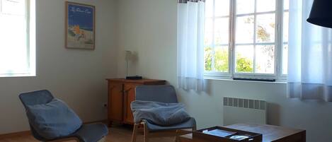 A room with a bed, two armchairs, a wooden table, a radiator, and a window with curtains.