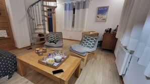A cozy living room with a wooden staircase, two armchairs with patterned cushions, a coffee table with snacks, and a framed picture on the wall. - Charmante maison au coeur du village /Charming house in the heart of the village (Wissant)