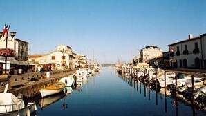 A marina with boats docked along the sides, a clear sky, and buildings with balconies and awnings.
